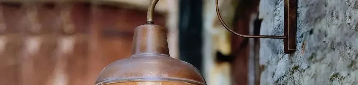 Antique brass wall light with a curved arm and dome shade mounted on a rustic stone exterior wall