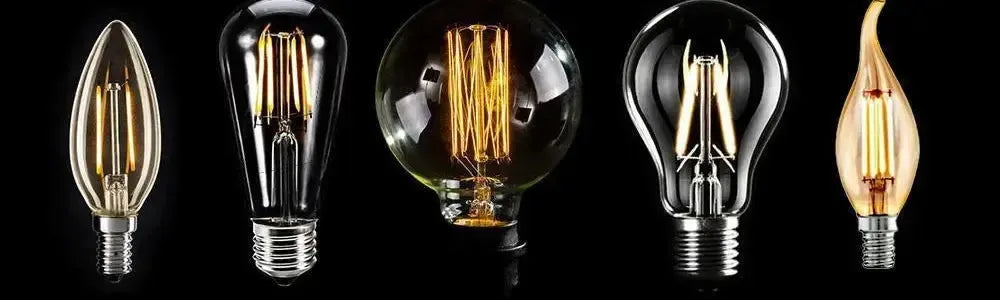 Assorted clear glass carbon filament globes in candle, pear, and round shapes with visible glowing filaments on black