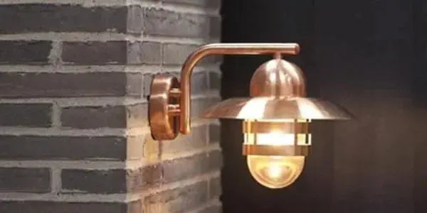 Copper wall light with a domed shade and protective cage mounted on a grey brick exterior wall