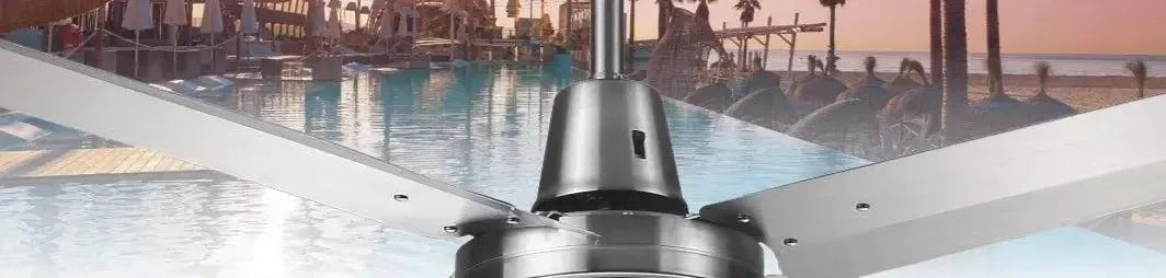 Brushed silver metal ceiling fan with four flat blades mounted against a tropical beach resort background