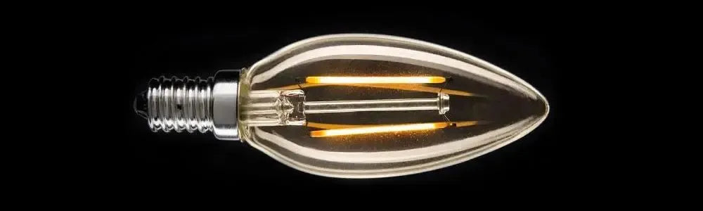 Clear glass candle shaped E14 globe with visible glowing yellow filaments and a silver screw base on a black background