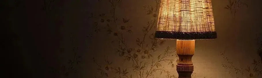 Timber table lamp with a textured fabric shade and turned wooden base against a vintage floral wallpaper background