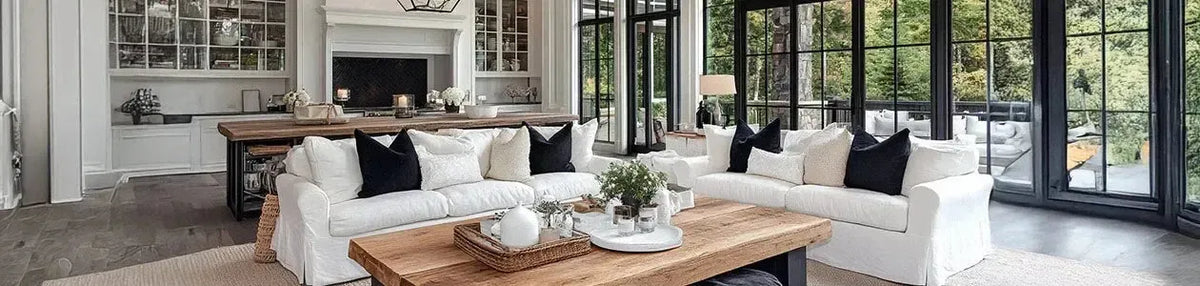 Elegant Hamptons living room with white slipcovered sofas, black accents, and large windows overlooking a garden