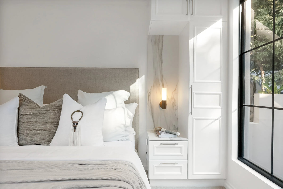 Modern cylindrical wall lamp with a black finish mounted on a marble panel beside a white bedroom wardrobe