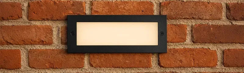 Rectangular black recessed brick light with a warm glow mounted into a rustic red brick wall