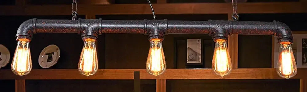 Black pipe pendant light with five exposed Edison bulbs suspended by chains against a dark timber shelving background