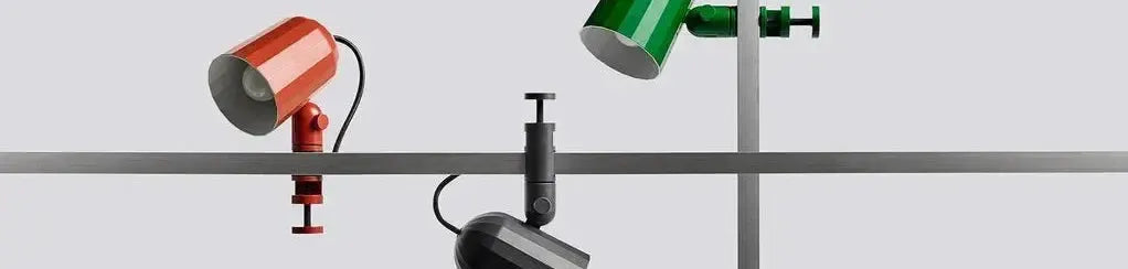 Glossy red, green and black cylindrical clamp lamps attached to a metal shelf frame against a plain background