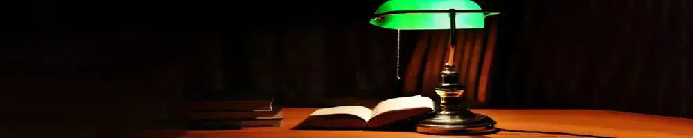 Classic green glass bankers lamp with a polished brass base illuminating an open book on a dark wooden desk