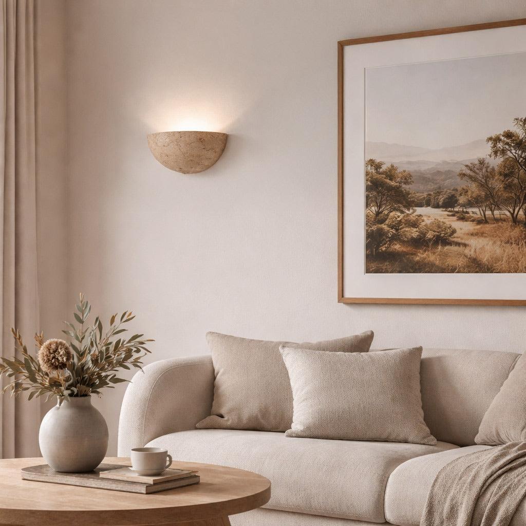 Gotico half-bowl travertine wall light casting a warm upward glow in a neutral-toned living room setting.