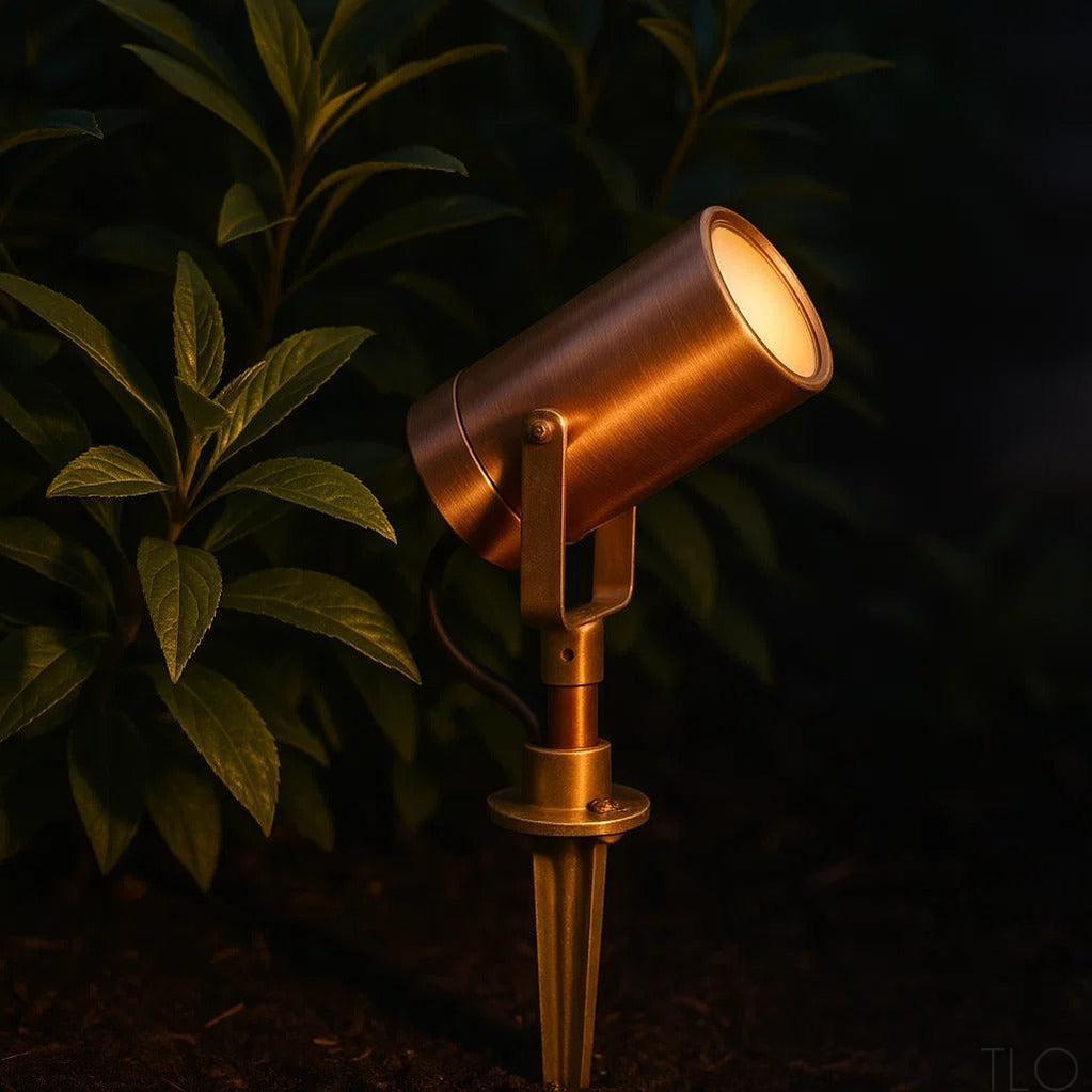 Outdoor copper spotlight with warm glow, illuminating dark green foliage.