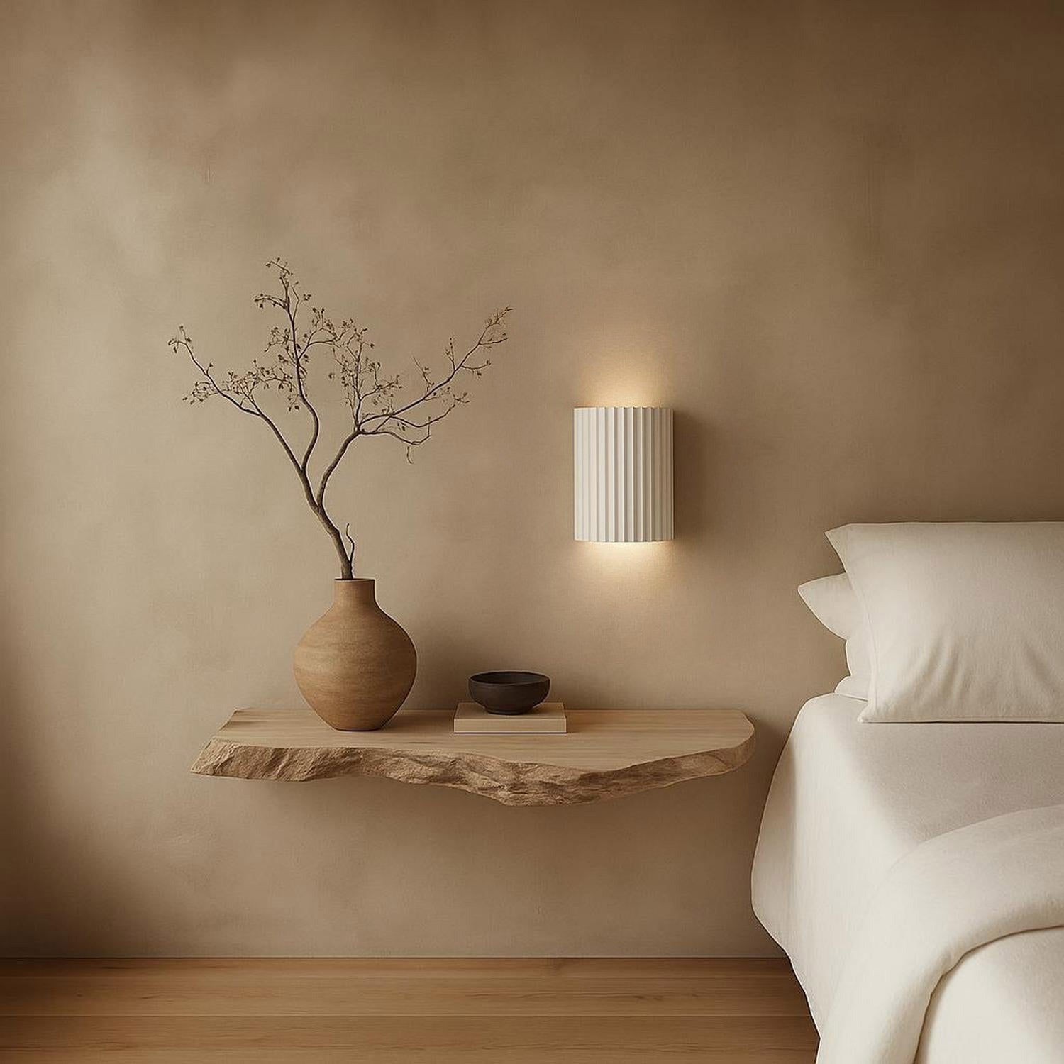 Ridged matte white plaster up/down wall light mounted above a wooden bedside shelf in a neutral bedroom.
