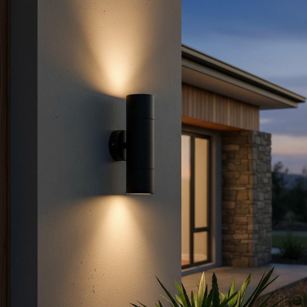 Cylindrical matte black LED up-down outdoor wall light mounted on a modern exterior pillar at dusk.
